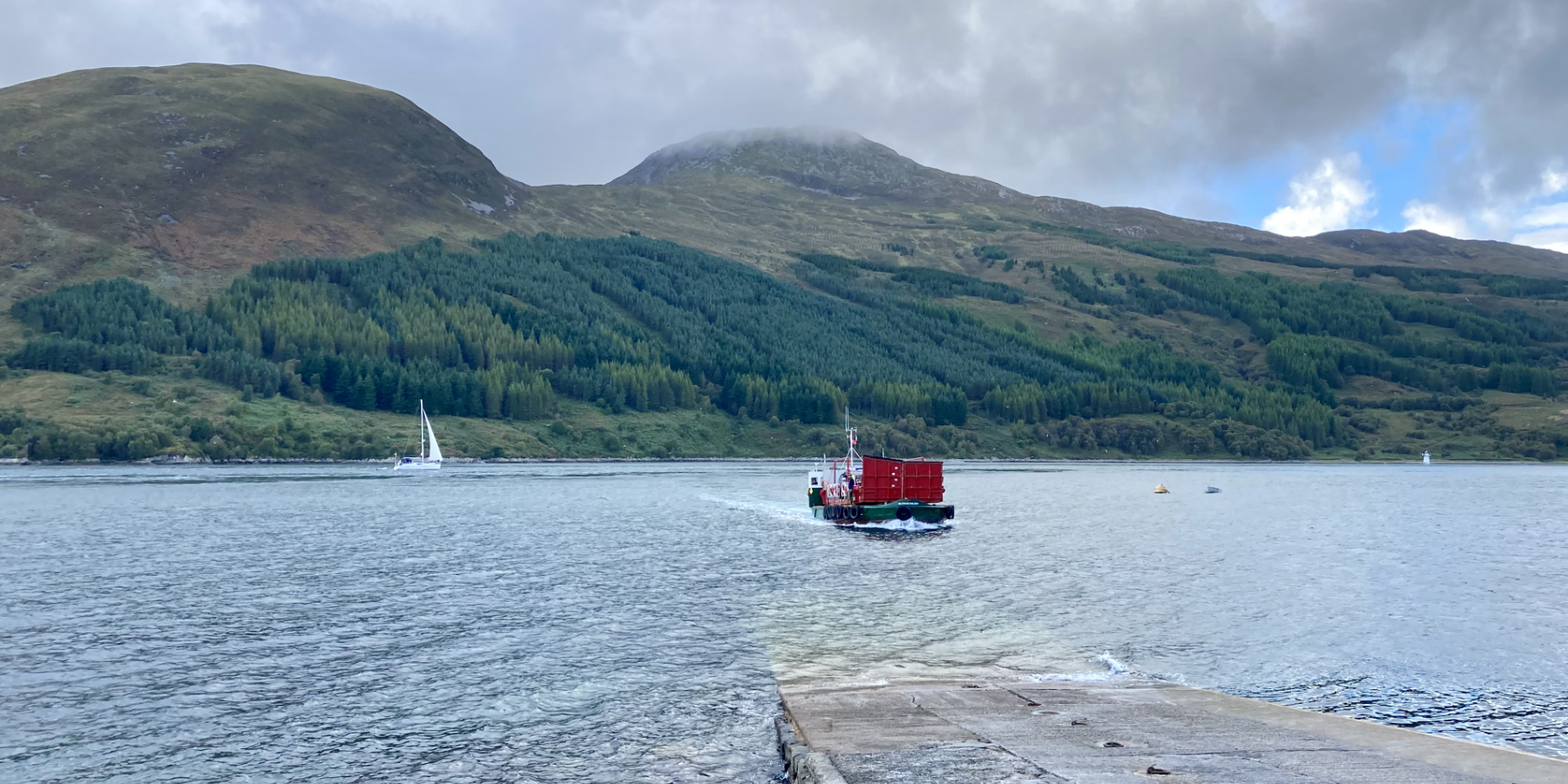 ferry approaching slip, cloudy day, fullish tide, yacht in background